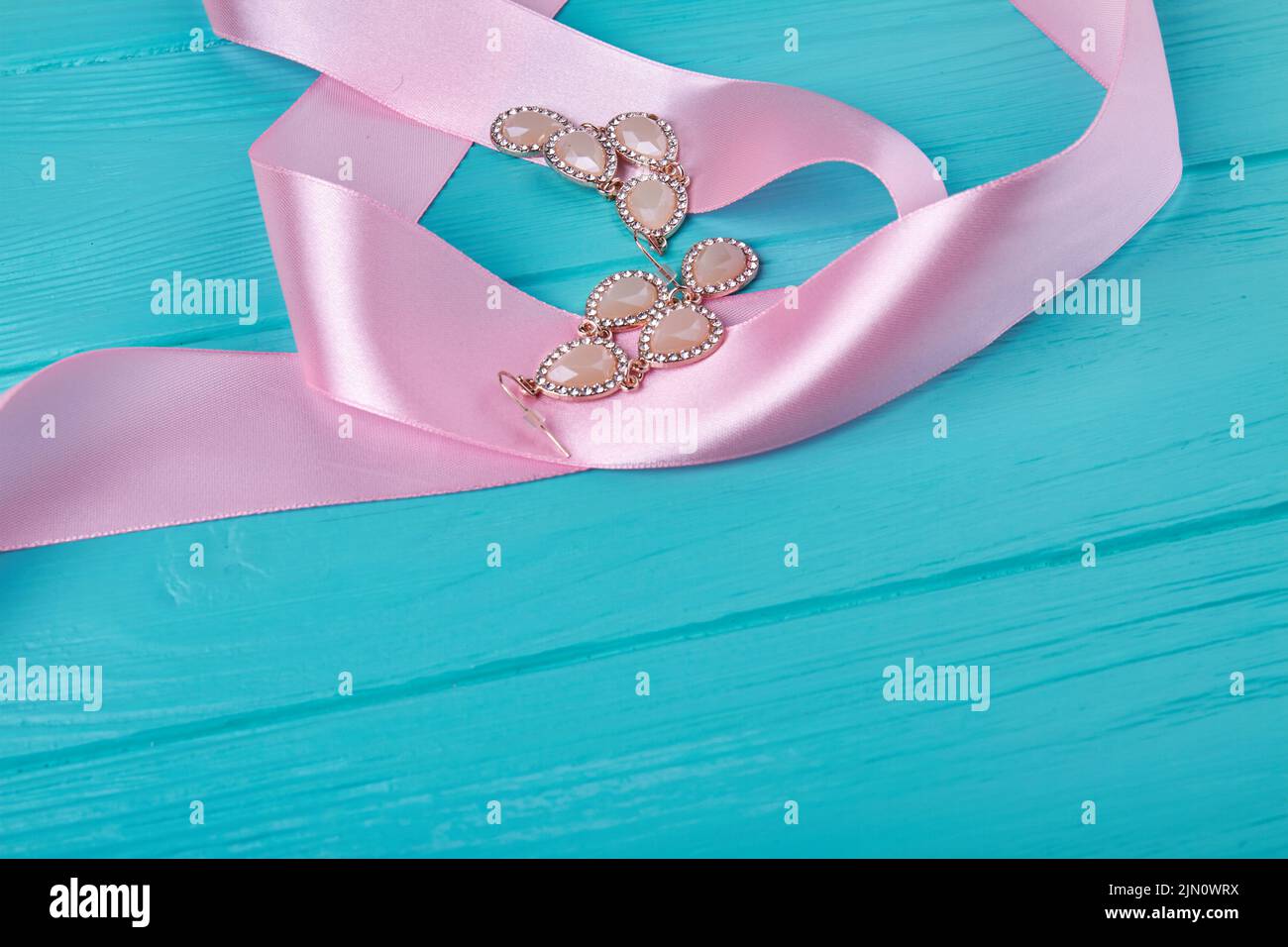Pink ribbon and earrings on blue wooden desk. Womens accessories and copy space. Stock Photo