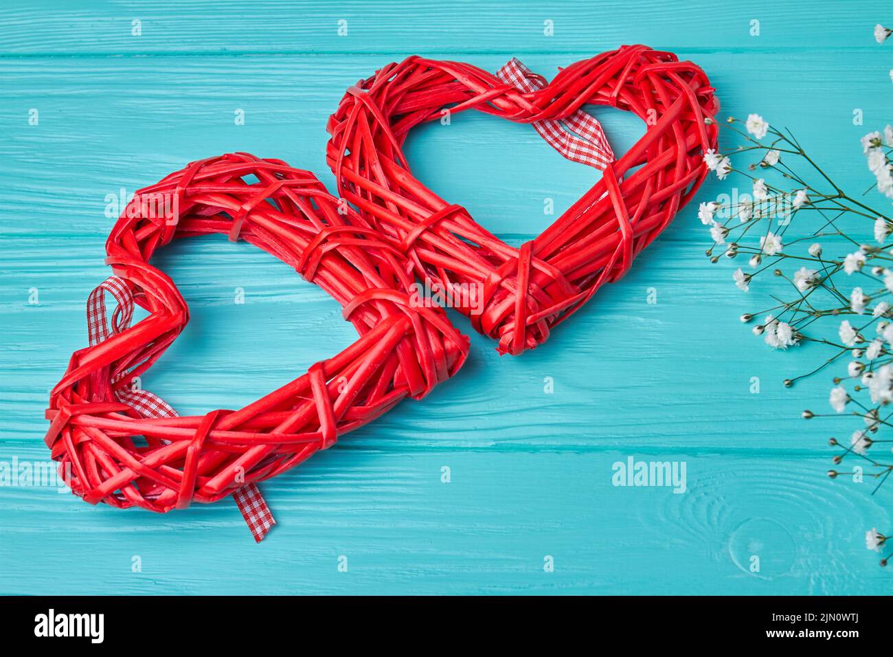 Two red wicker hearts on blue wooden desk. Tiny white flowers. Stock Photo