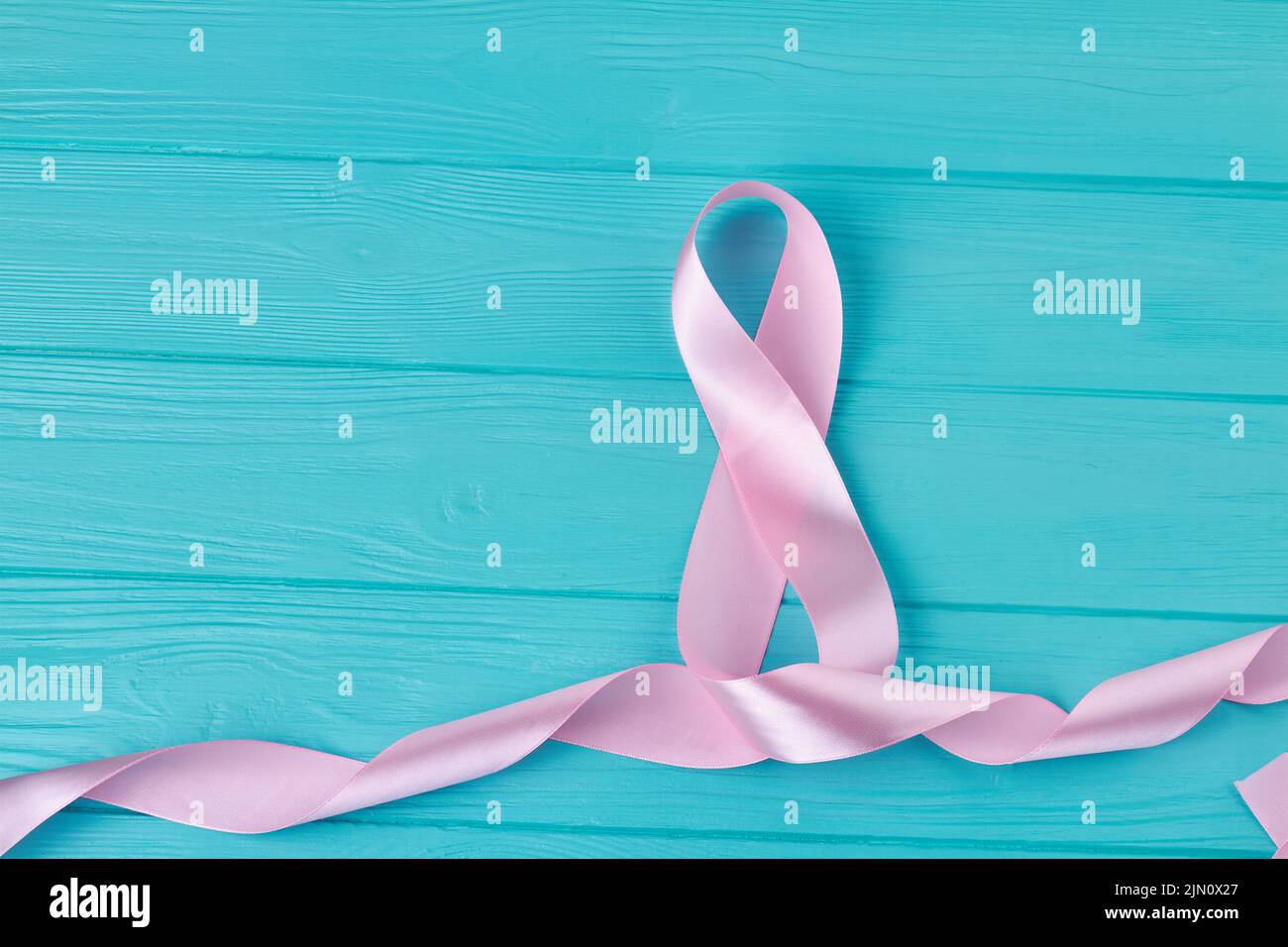 Pink silk ribbon tape in the shape of eight. Blue wooden desk. Stock Photo