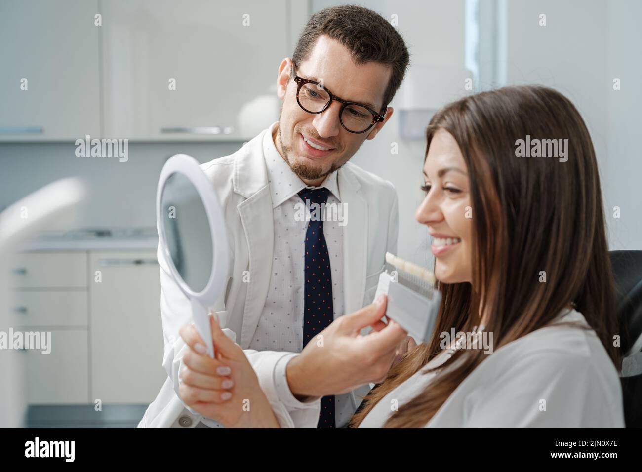 Young man dentist in white coat show veneers enamel color palette for