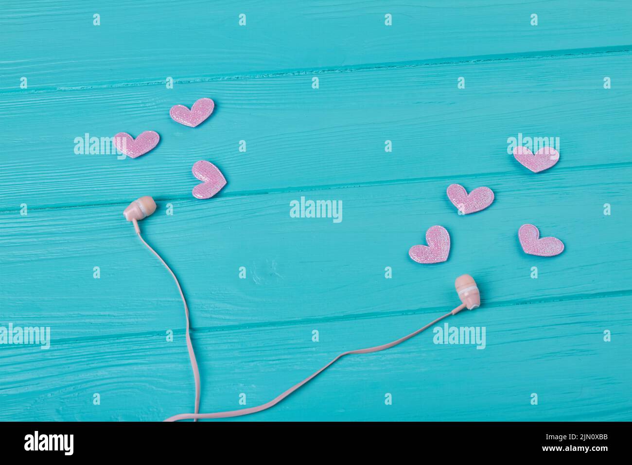 Earphones and pink hearts on blue wooden desk. Love music concept. Stock Photo