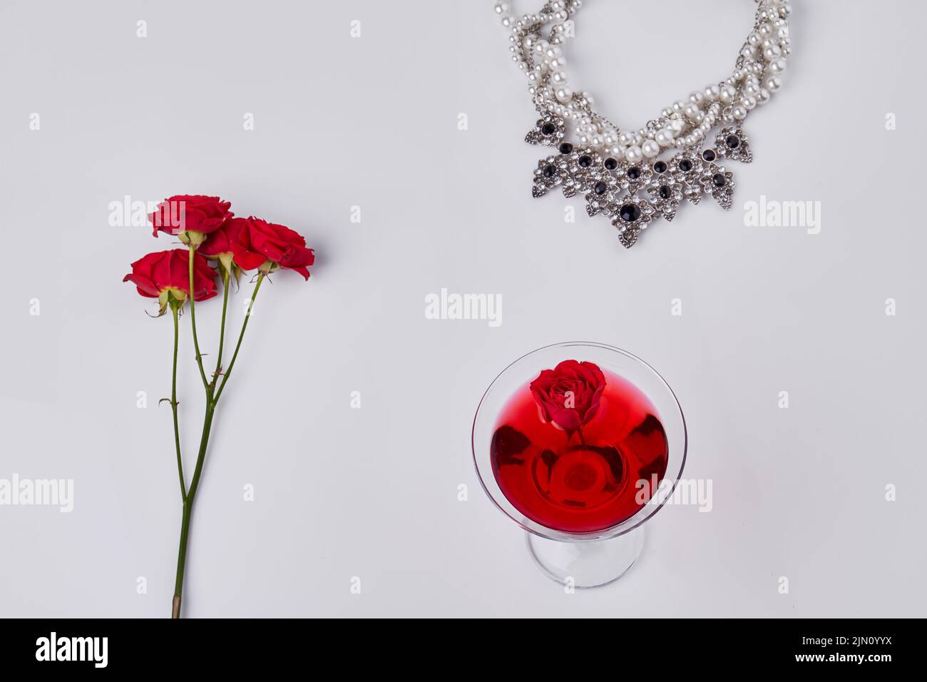 Red cocktail with rose flowers and neckalce. Top view flat lay. Isolated on white. Stock Photo