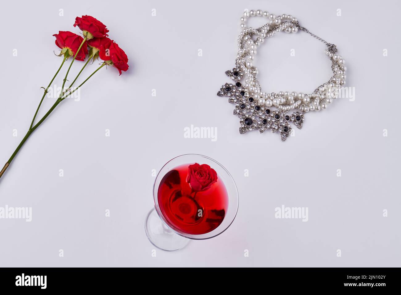 Flat lay womens accessories on white background. Red cocktail with rose flowers and necklace. Stock Photo