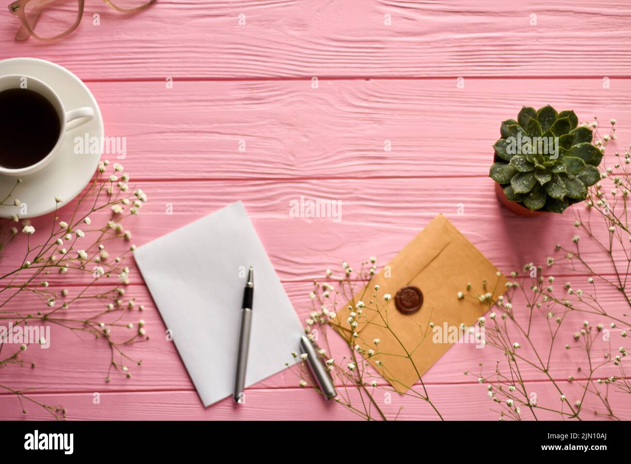 Top view workdesk accessories on pink wooden desk. Blank paper with pen and envelope. Stock Photo