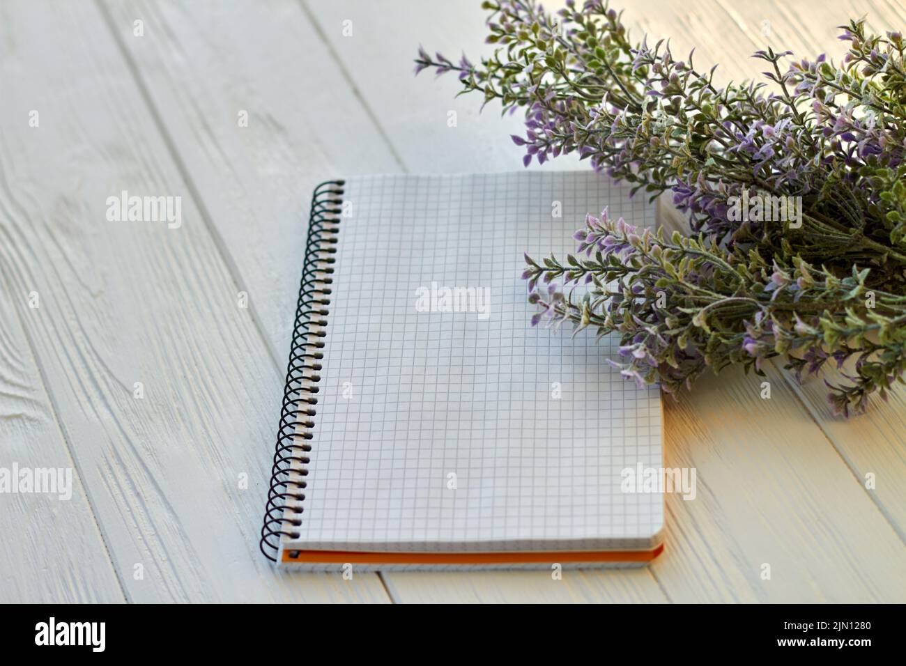 Blank notepad and purple flowers on wooden desk. Checkered page for copy space. Stock Photo