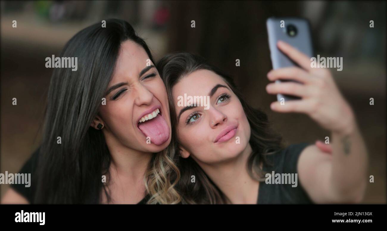 Girlfriends Taking Selfie Sticking Tongue Out Young Women Posing For Photo Holding Smartphone 