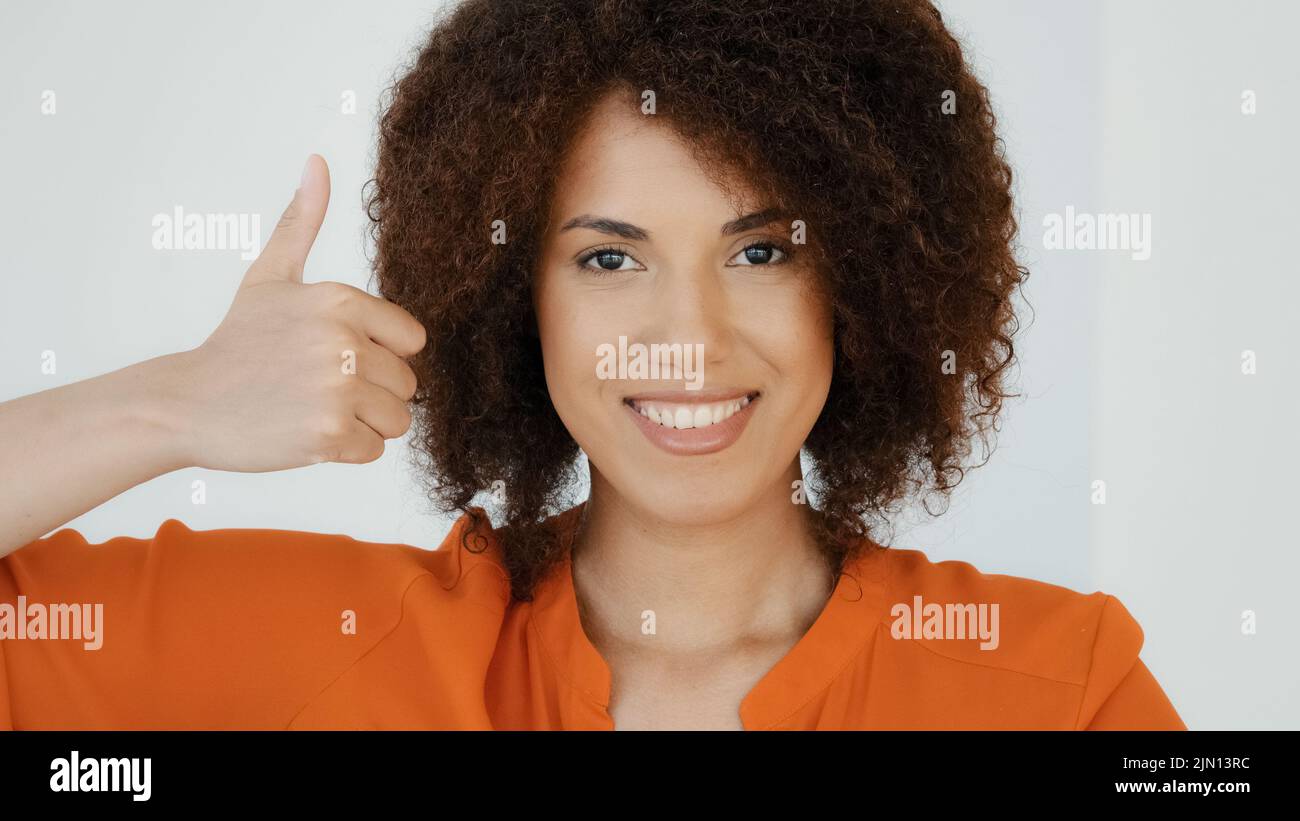 Smiling cheerful African American happy woman with curly hairstyle showing thumb up looking at camera enjoying positive feedbake proud winner female Stock Photo