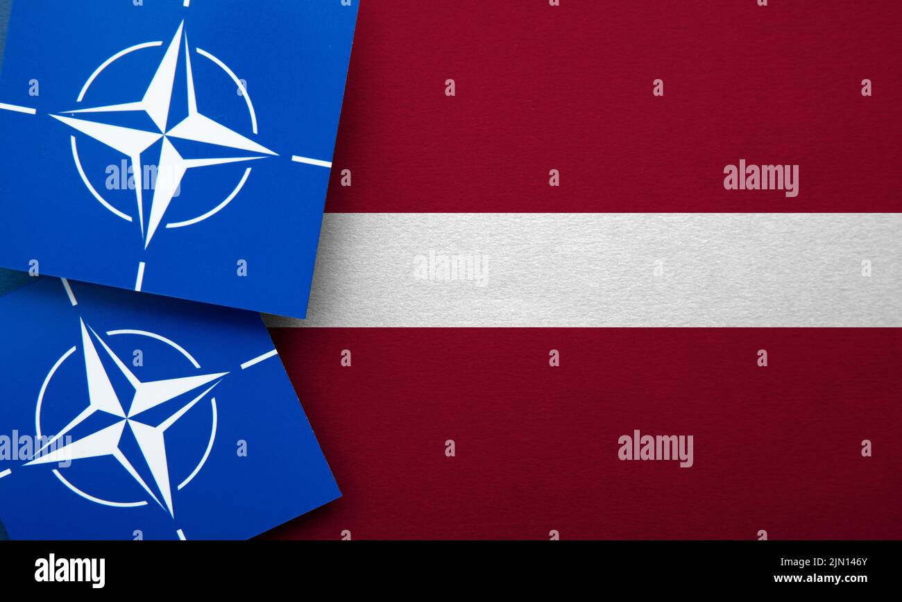 LONDON, UK - August 2022: NATO North Atlantic Treaty Organization military alliance logo on a Latvia flag Stock Photo