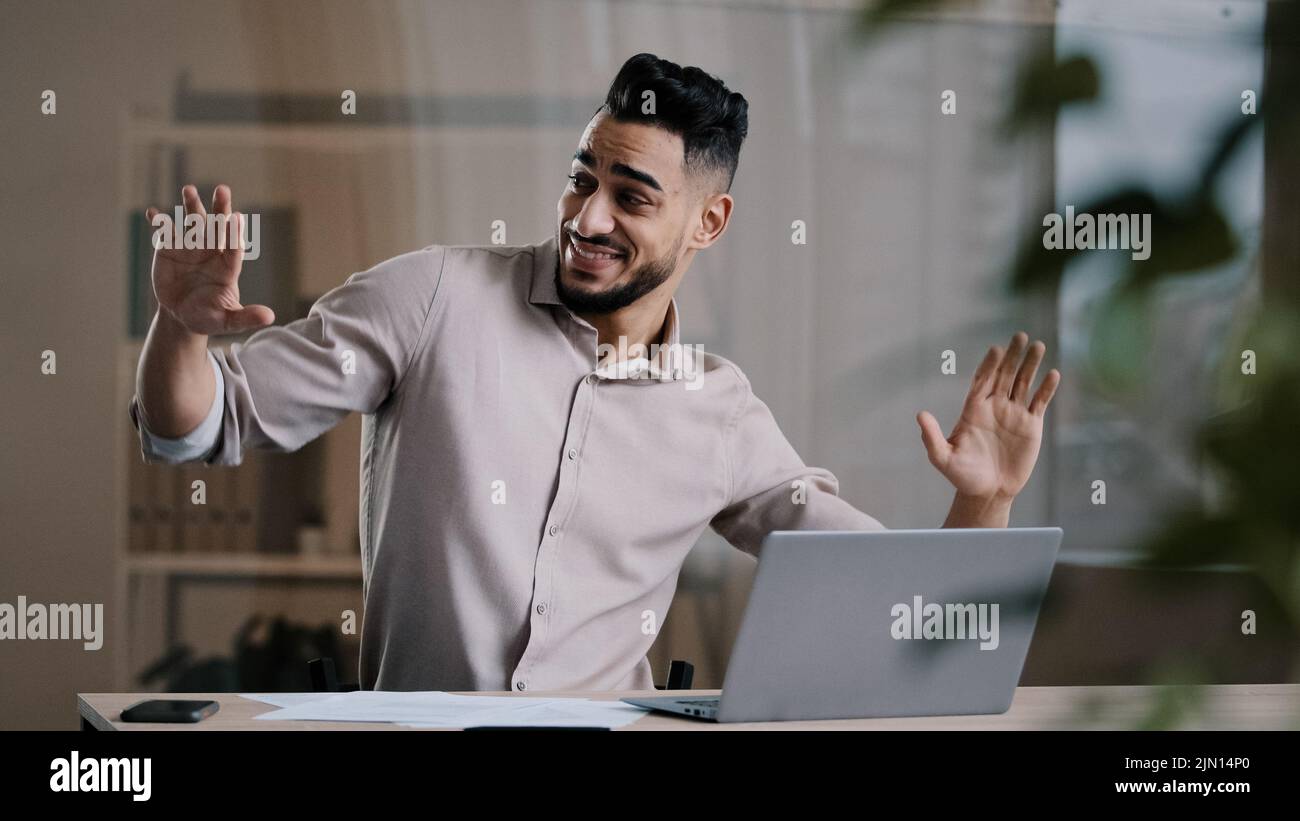 Happy funny male arabic businessman hispanic young guy millennial smiling man active dancing at home office has fun celebrate end of working enjoy Stock Photo