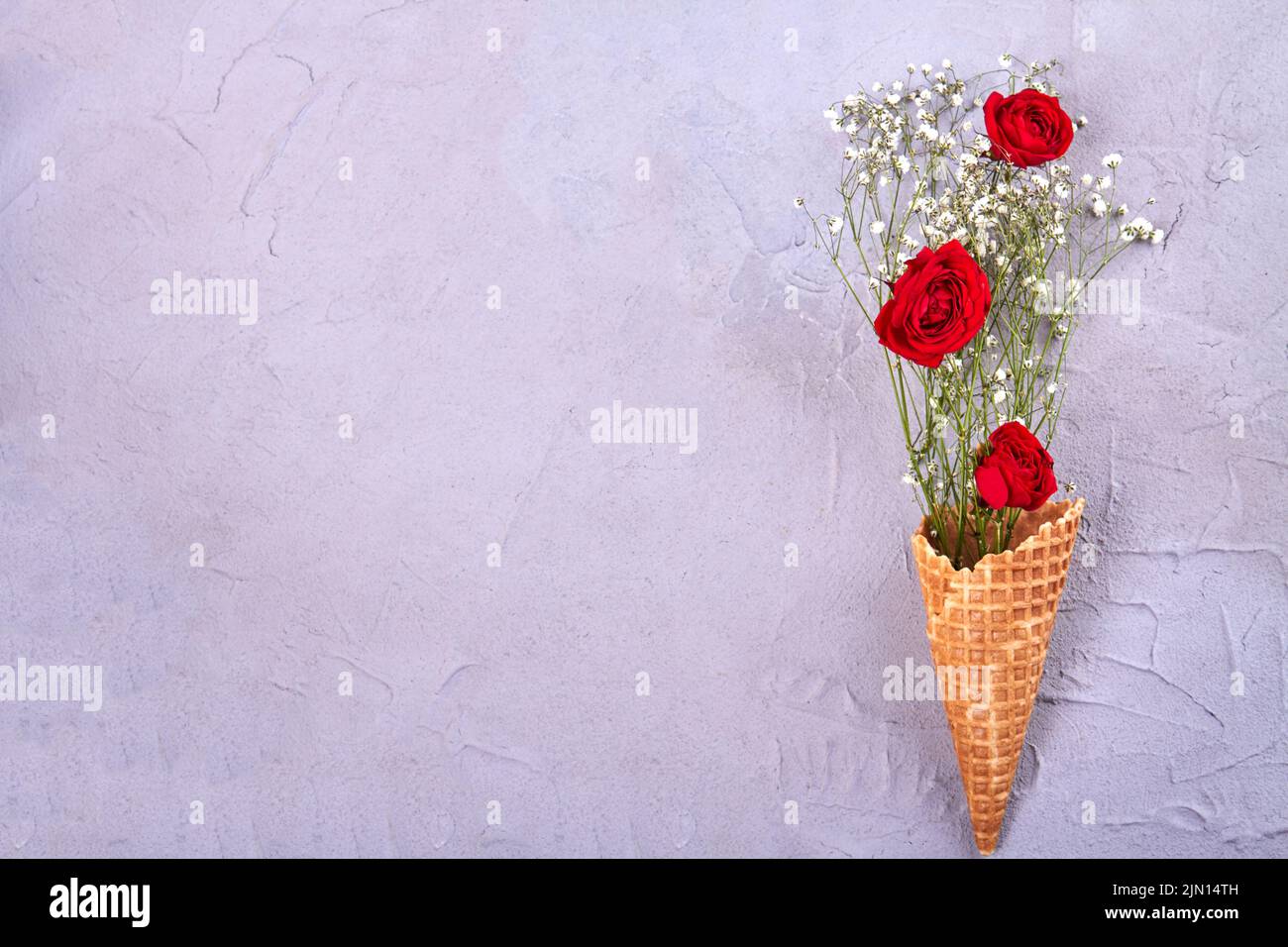 Waffle ice cream cone with flowers and copy space. Red roses and tiny white flowers. Stock Photo