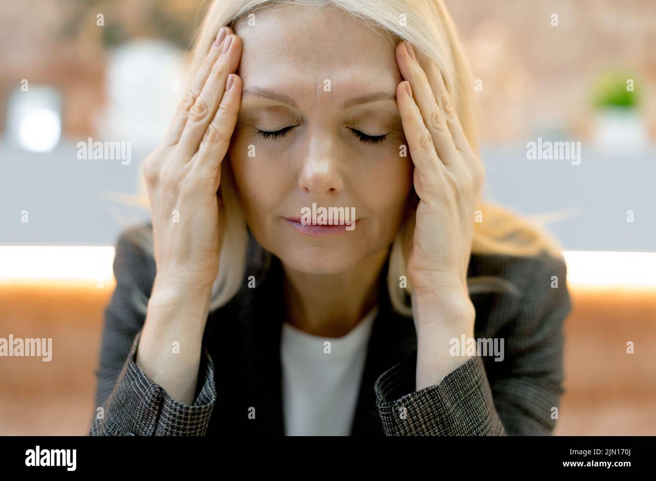 Close-up of a tired exhausted middle aged caucasian business lady, experiencing fatigue from work, overwork, suffering from headache, migraine, massages her temples, closed her eyes, needs rest Stock Photo