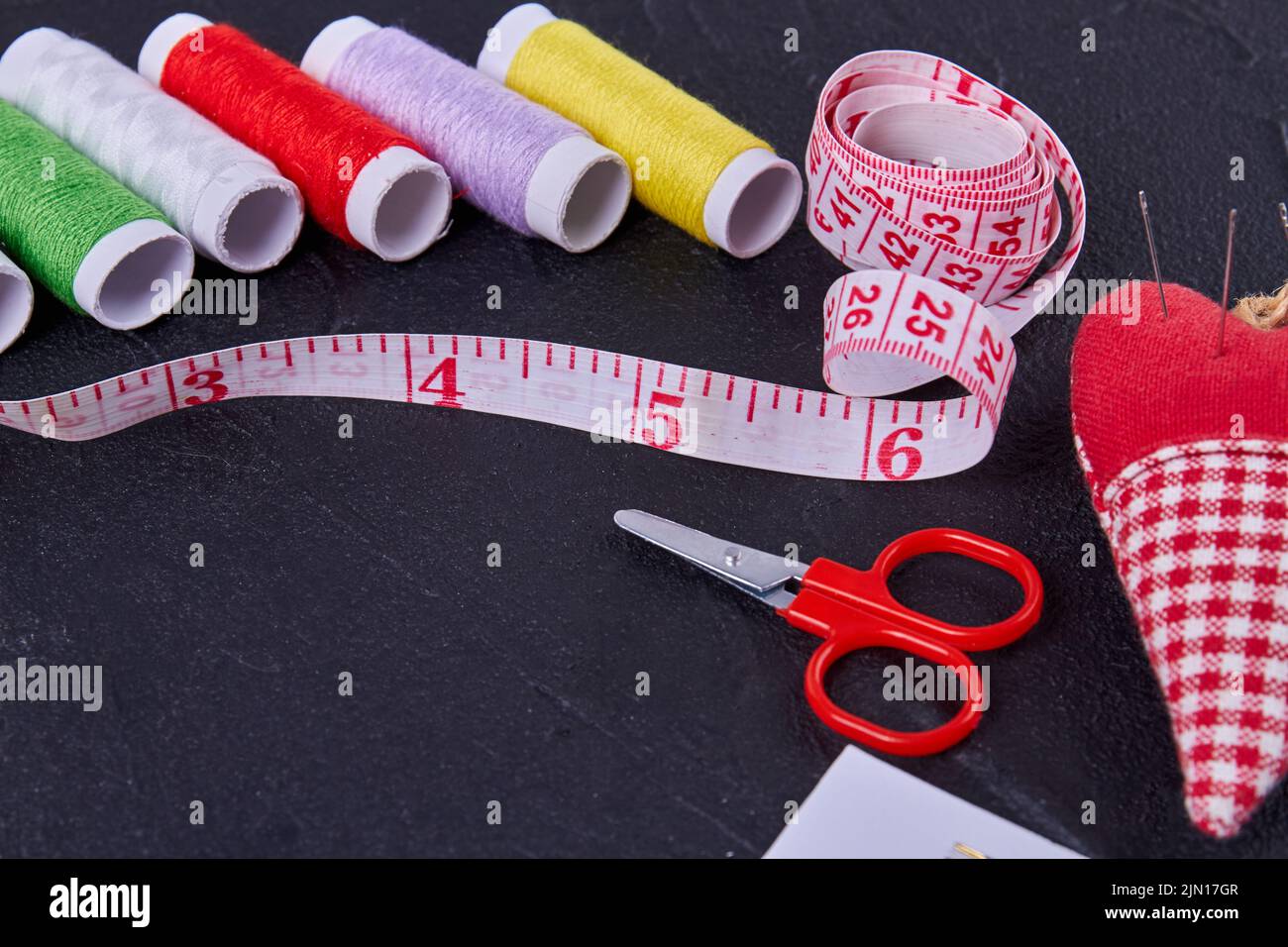 Close up set of sewing accessories on dark surface. Threads with measure tape and scissors. Stock Photo