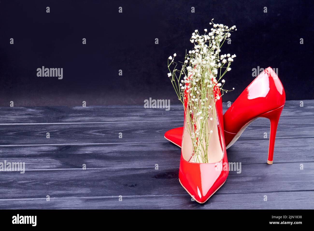 Pair of red high heel shoes with white flowers. Dark background with copy space. Stock Photo