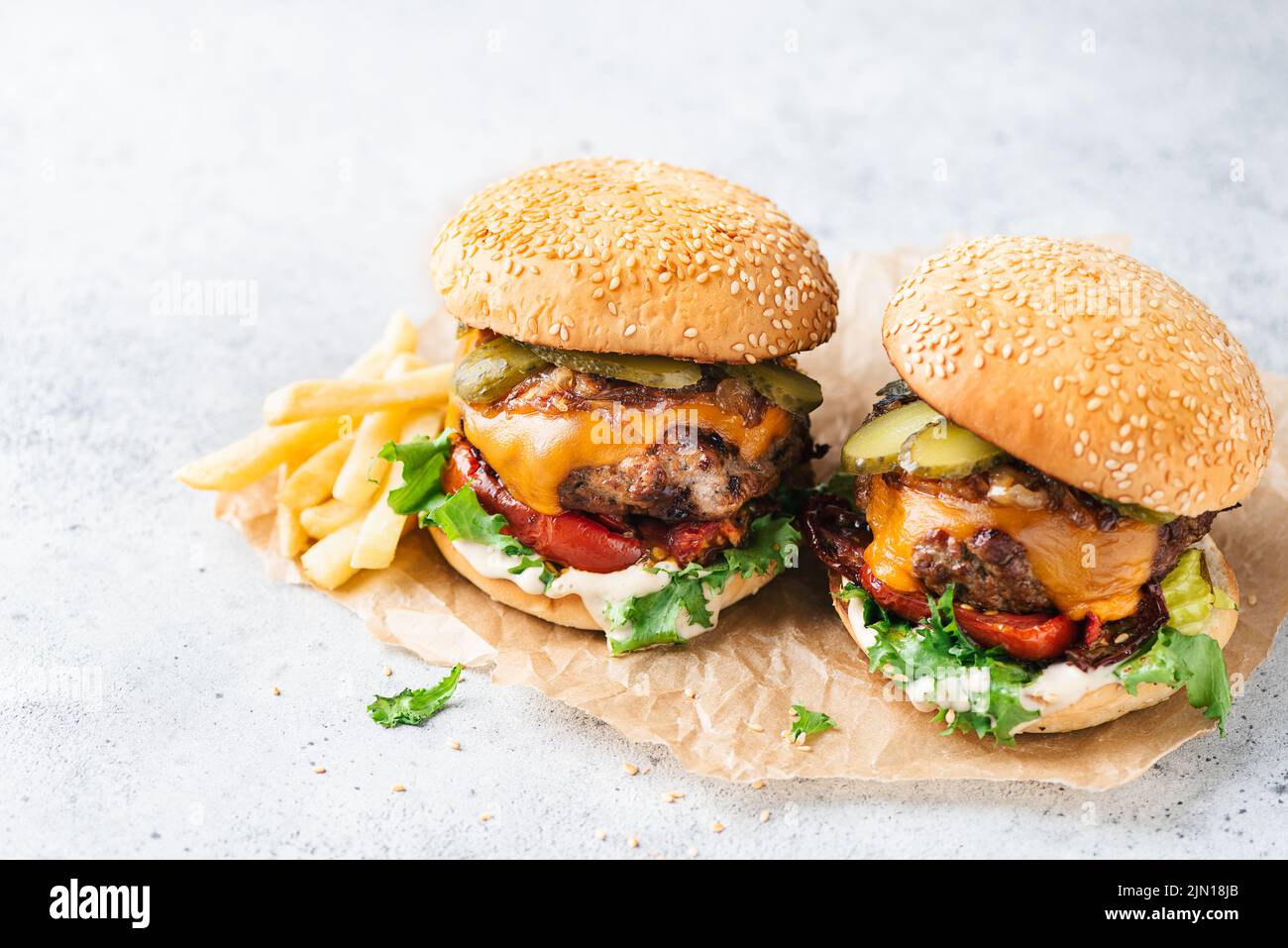 Cheeseburger with grilled red bell pepper, arugula and dill pickles served on parchment paper. Grey stone backgdrop Stock Photo