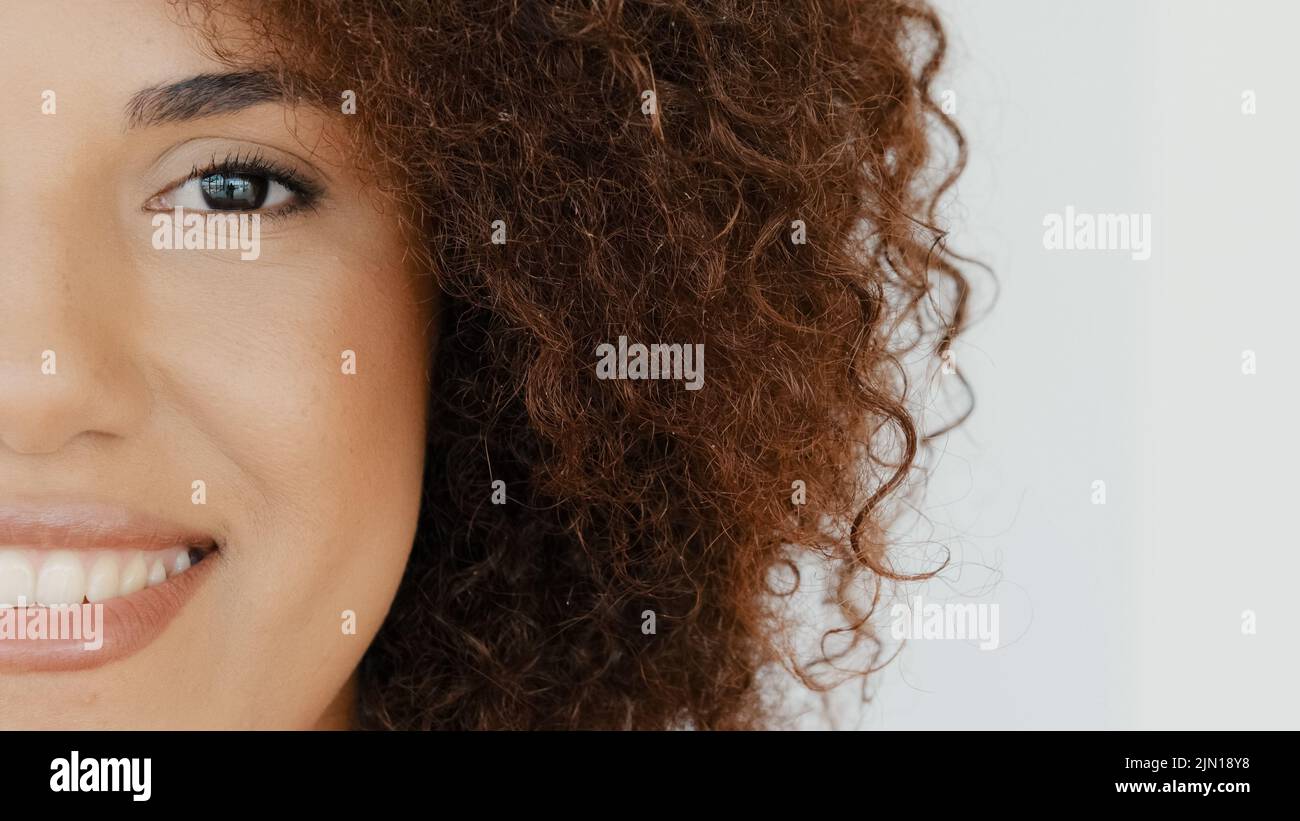 Close up young african american smiling toothy happy curly hair woman face half opening eye and looking to camera with smile. Portrait of pretty Stock Photo
