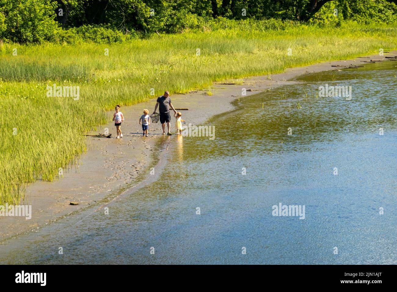 father and children walking along the rivers edge of the Kennebec river in Hallowell Maine Stock Photo