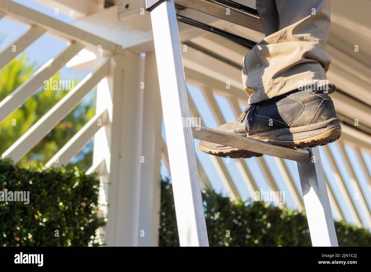 Close up view of faceless person climbing the ladder while working on the roof of a house. Security shoe at work concept with light Stock Photo