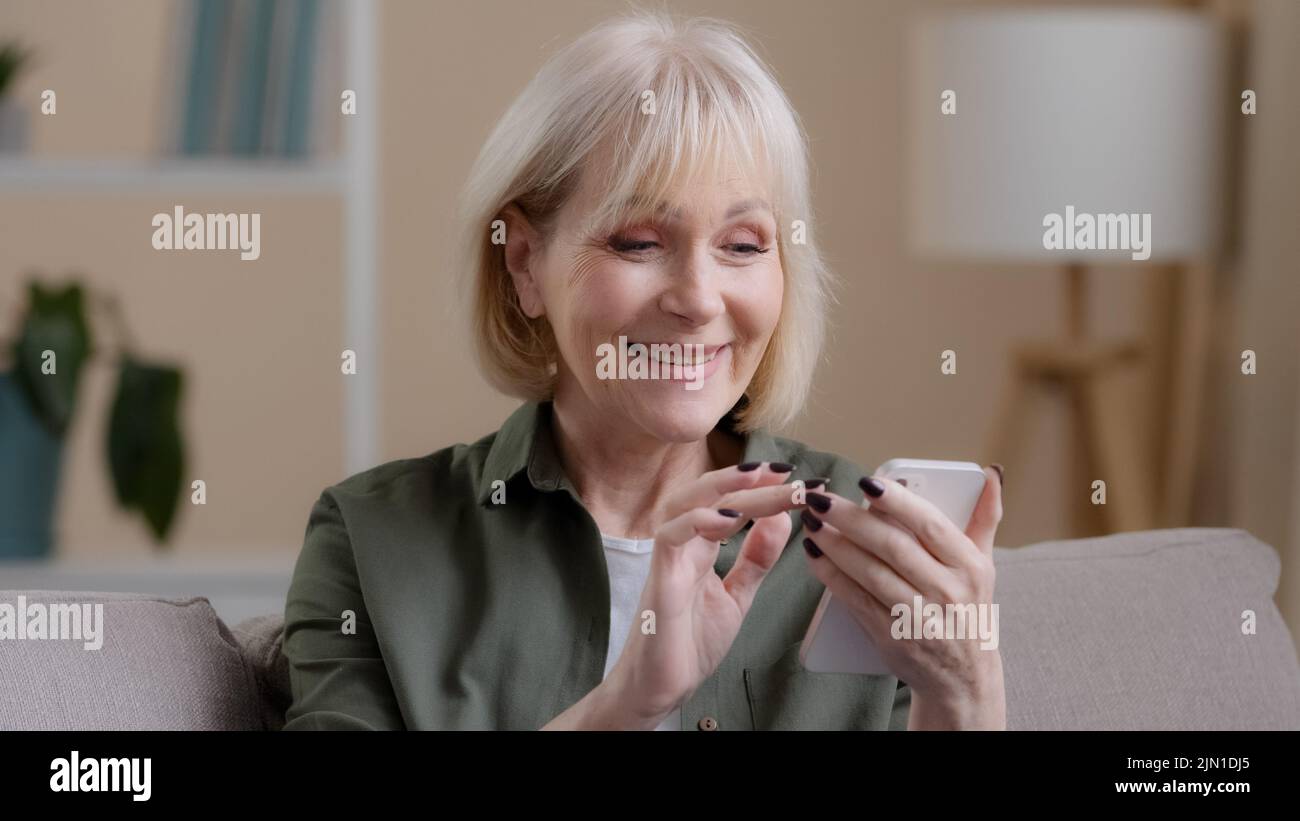 Close up happy excited successful amazed old emotional woman receive good news offer money prize achievement with phone smiling rejoice showing thumb Stock Photo