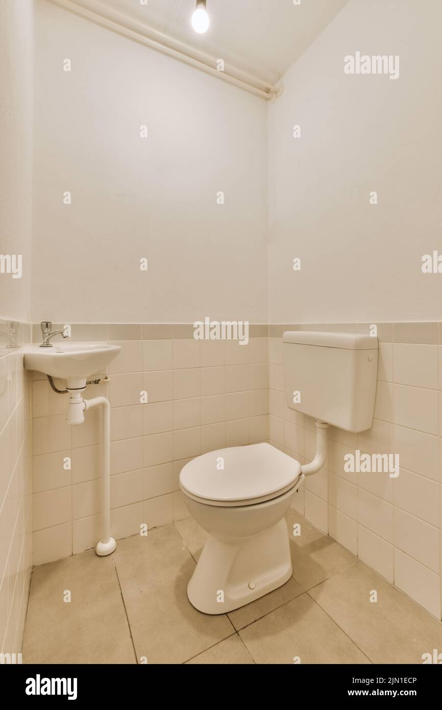 Wall hung toilet and small sink in corner in lavatory room with beige