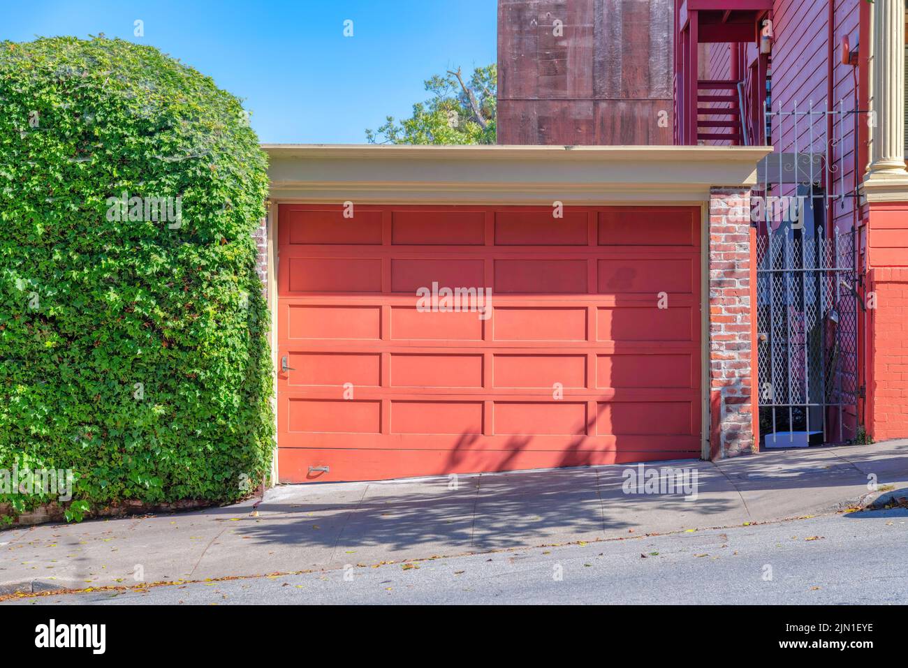 Detached garage exterior with peach wooden garage door at San Francisco, California. There is a shrub wall on the left of the garage and a gate on the Stock Photo