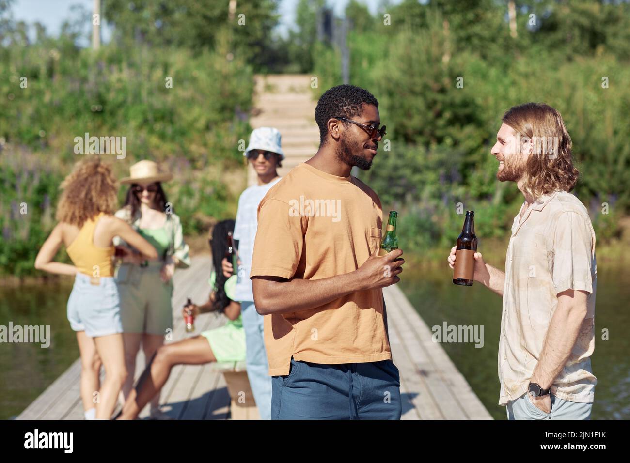 Side view portrait of two young men drinking beer outdoors in Summer and chatting Stock Photo