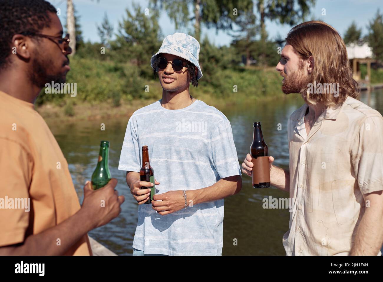 Waist up portrait of three young men drinking beer outdoors and chatting in Summer setting Stock Photo