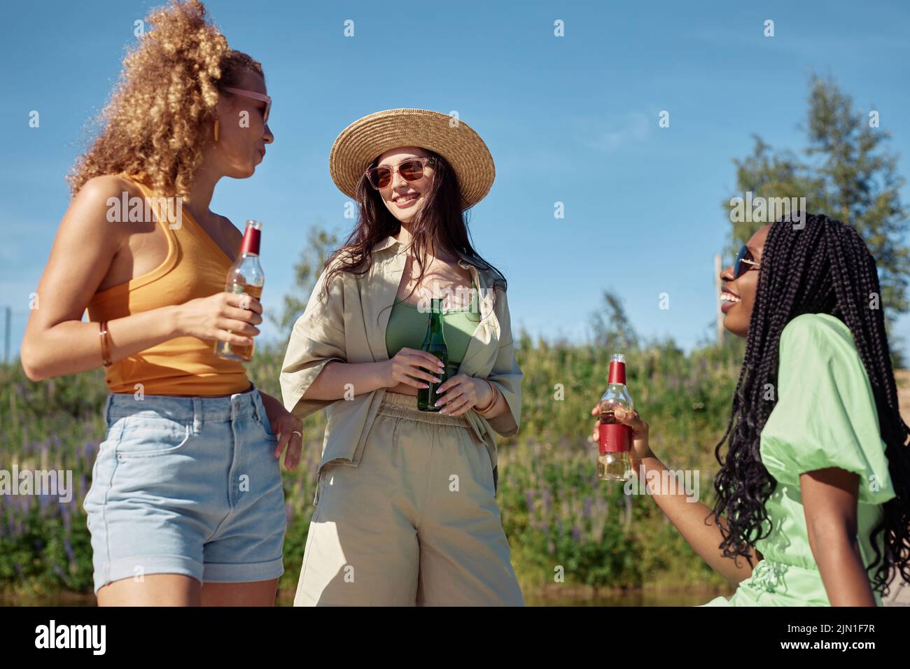 Diverse group of three young women enjoying refreshing drinks outdoors in Summer lit by sunlight Stock Photo
