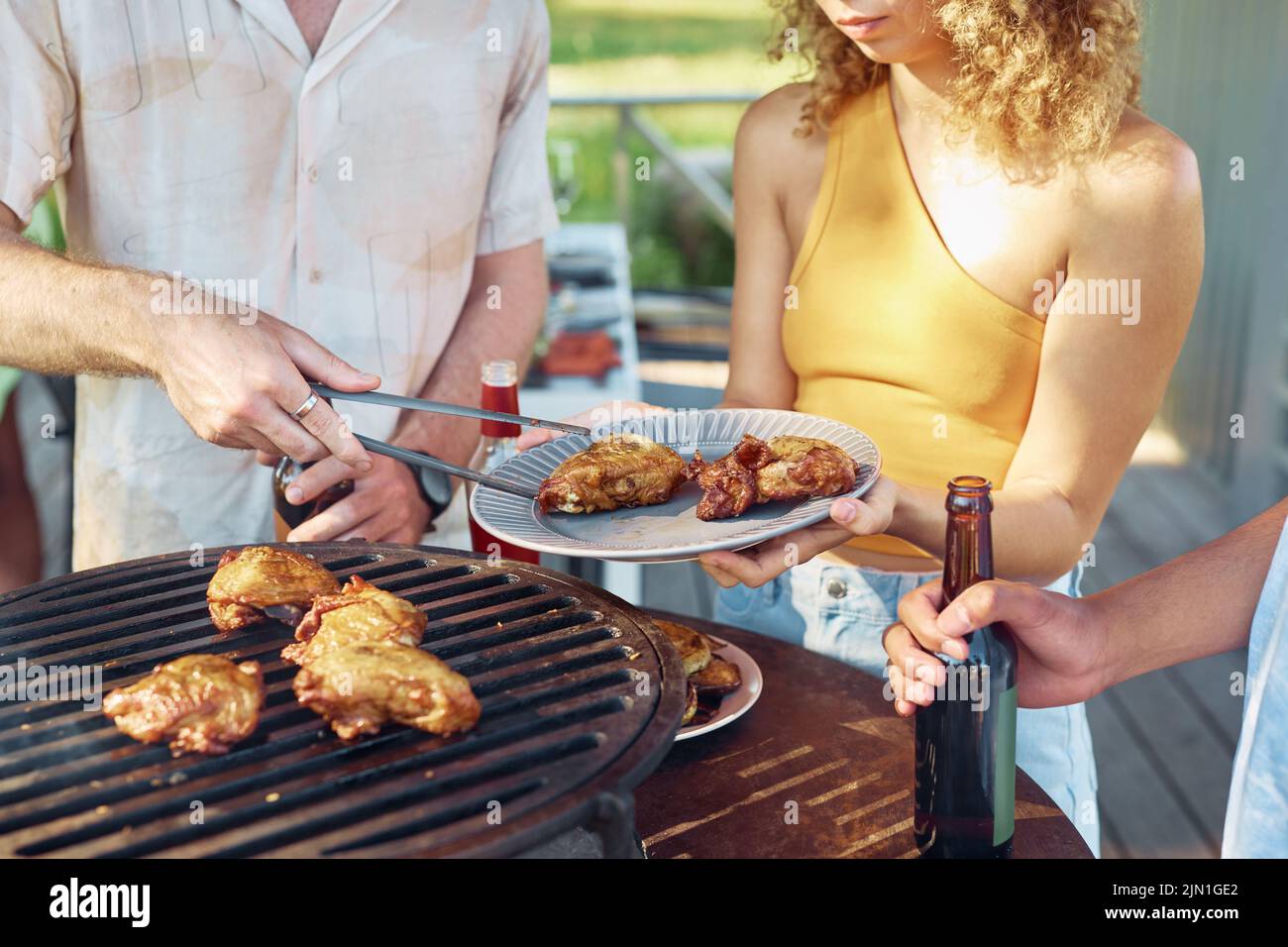 Close up of friends grilling chicken meat during barbeque party outdoors in Summer Stock Photo