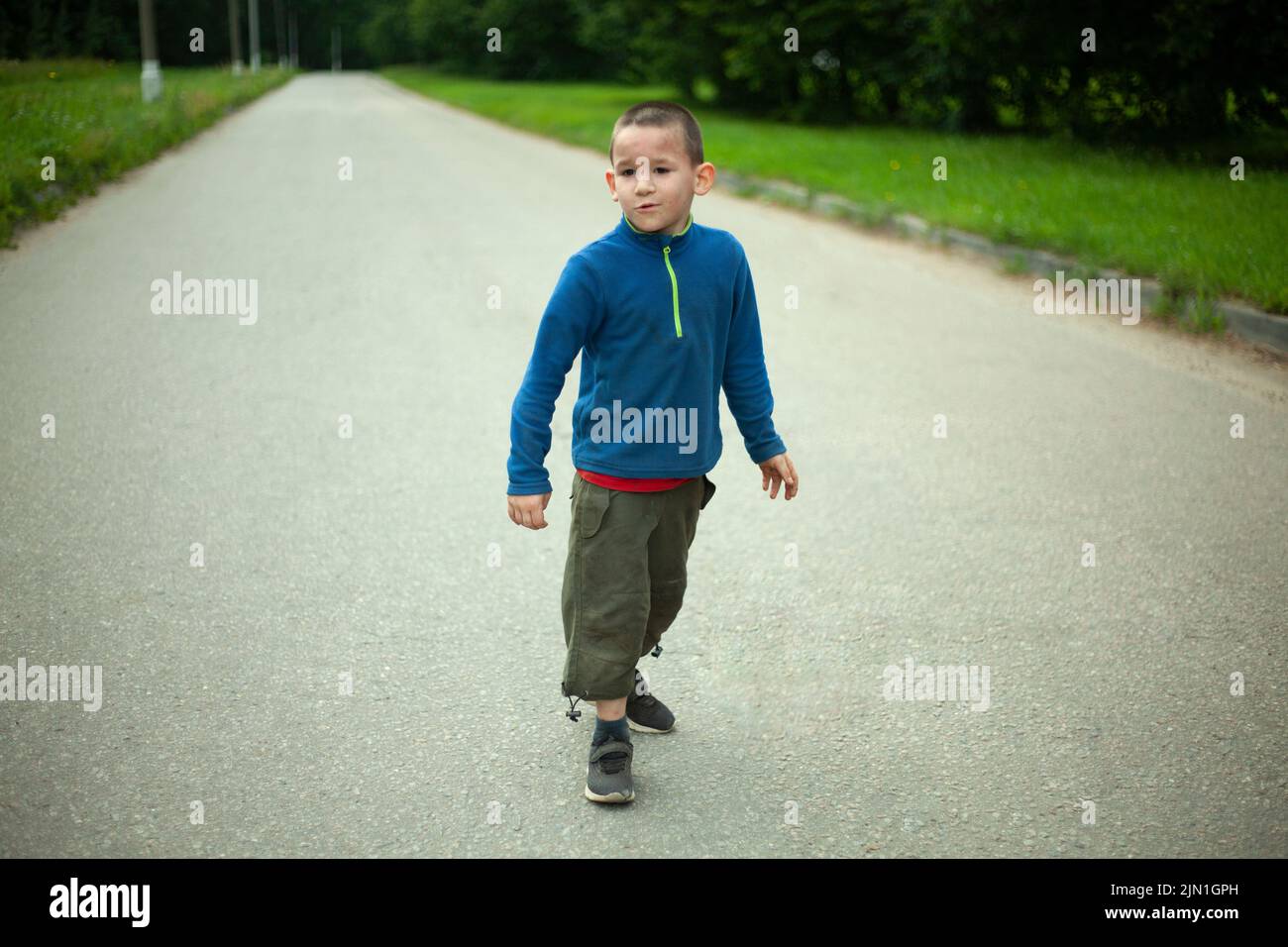 Child runs down road. Boy in summer. Schoolboy on street. Street boy in town. Stock Photo