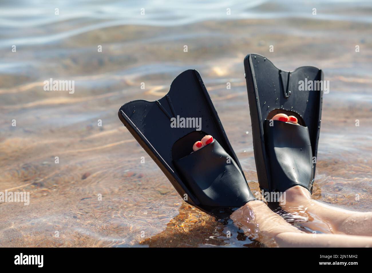A woman in black flippers splashes near the shore. Fins stick out of