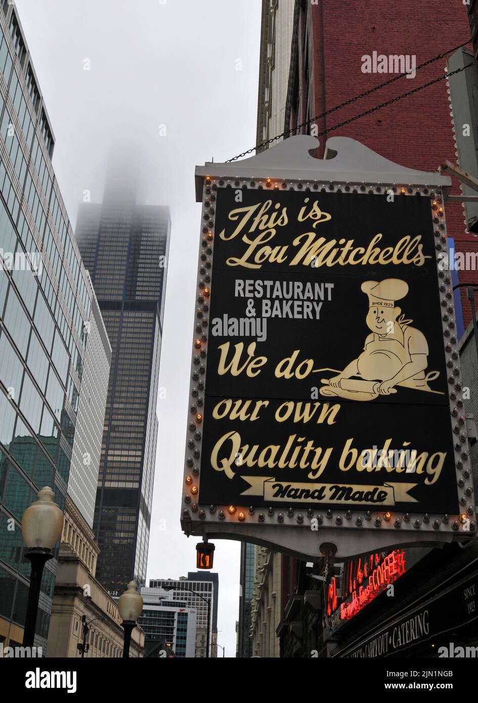 The sign for Lou Mitchell's, a restaurant that opened in 1923 in Chicago, IL is pictured near the fog-obscured Willis Tower (formerly Sears Tower). Stock Photo