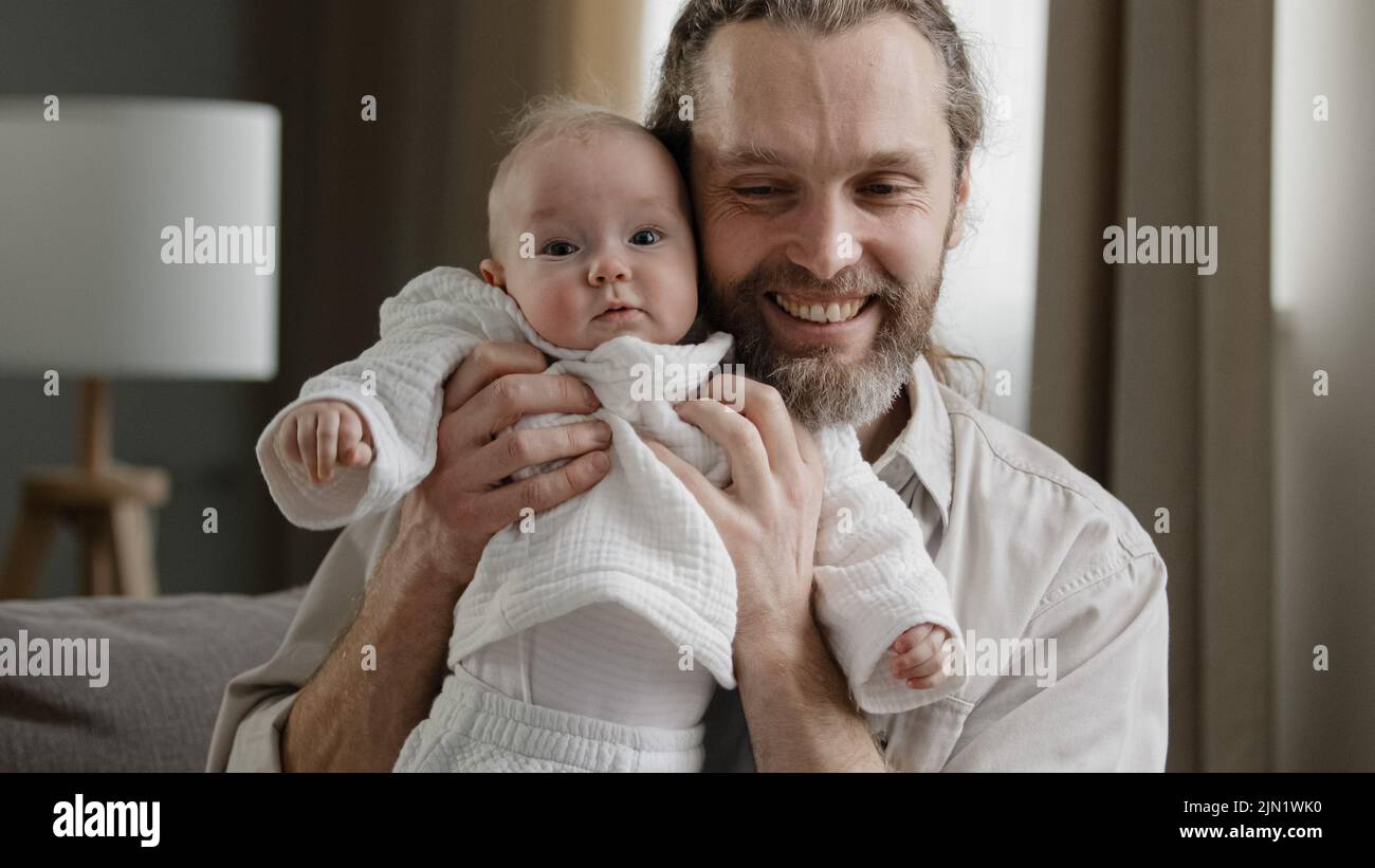 Loving adult bearded father holding baby newborn caring dad playing with little daughter son child jumping laughing man kissing kid in head together Stock Photo