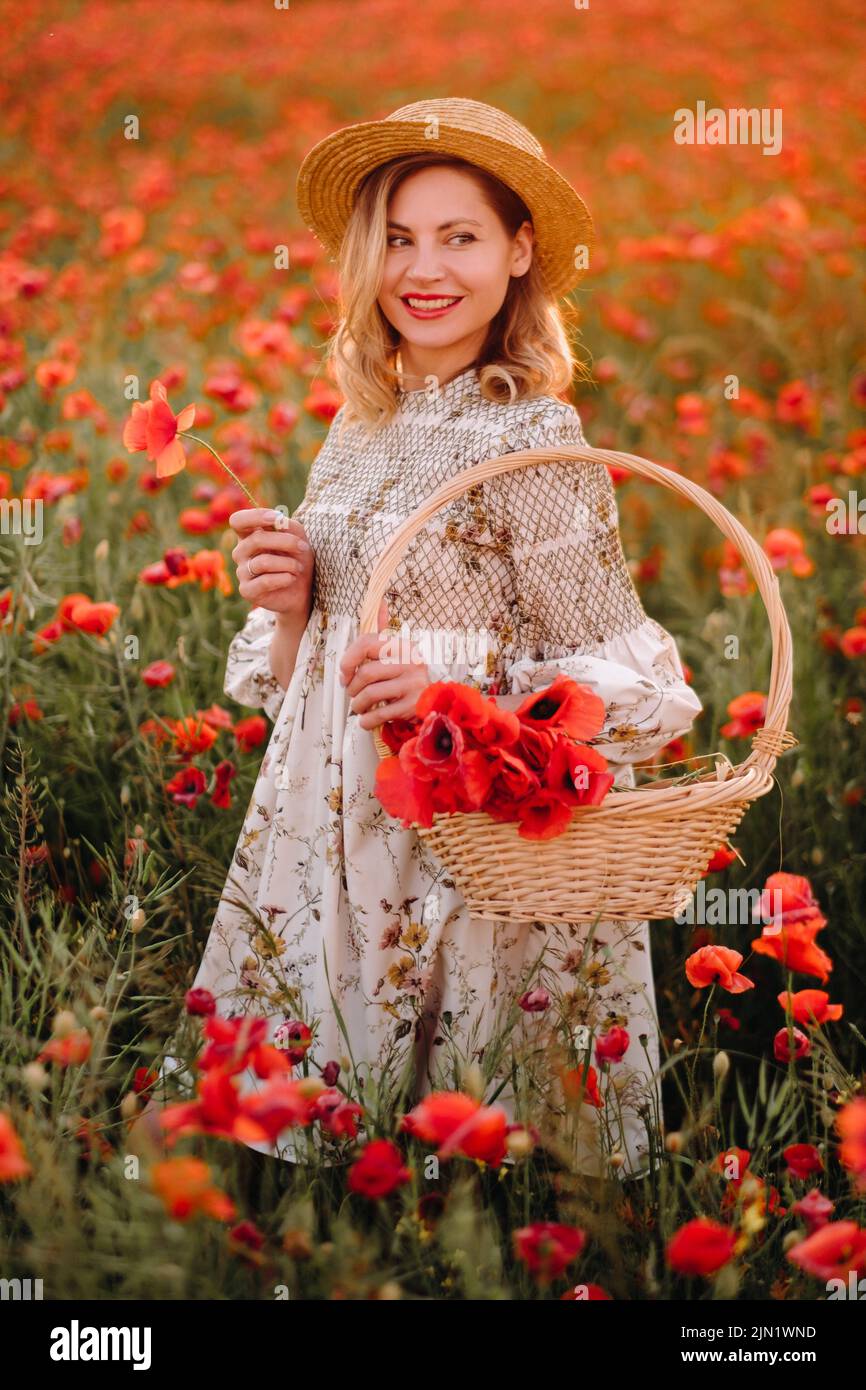 a girl in a dress with a hat and with a basket in a field with poppies ...