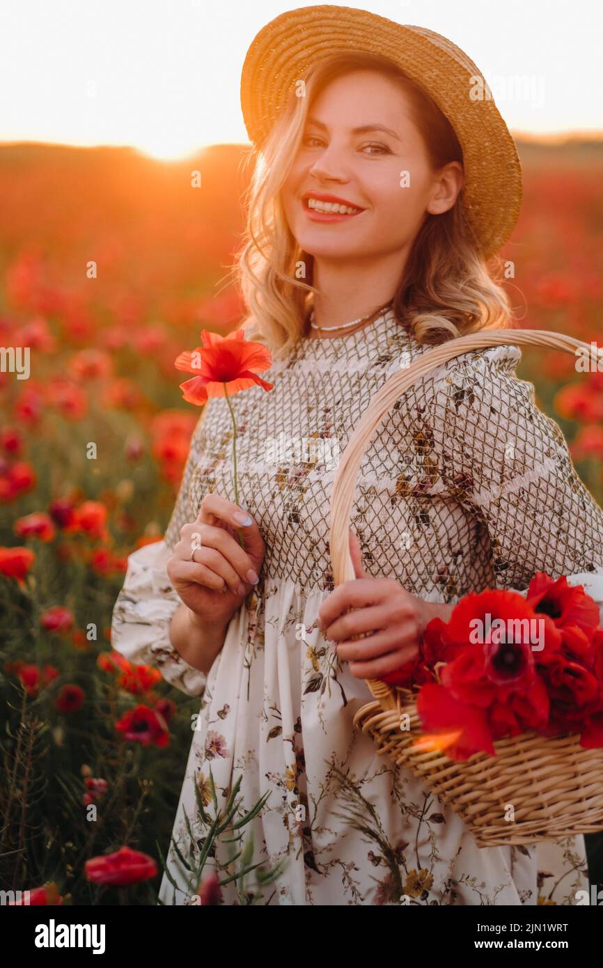 a girl in a dress with a hat and with a basket in a field with poppies. Stock Photo