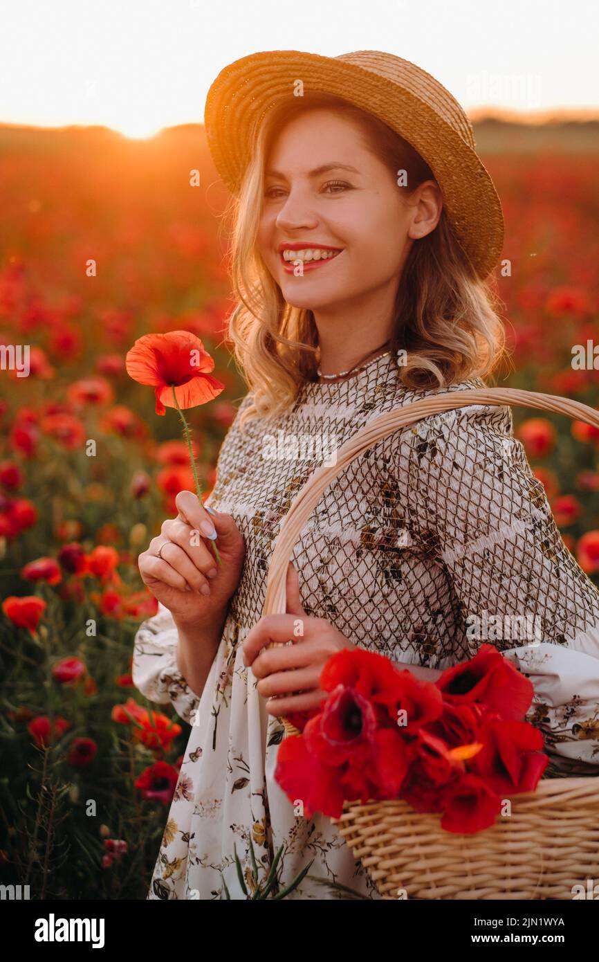 a girl in a dress with a hat and with a basket in a field with poppies ...