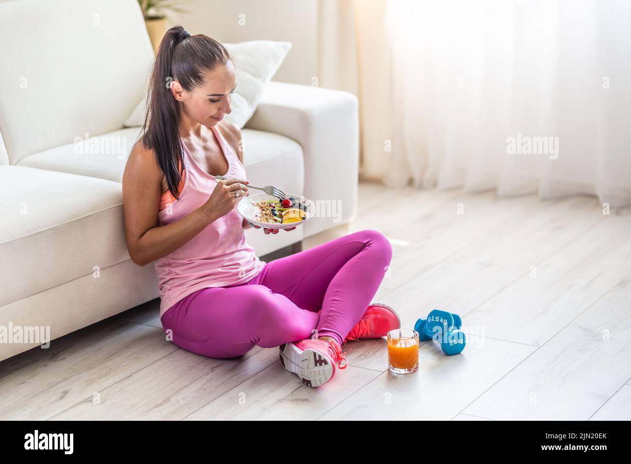 Sporty young woman eating a oatmeal with berries and fruits after a workout. Stock Photo