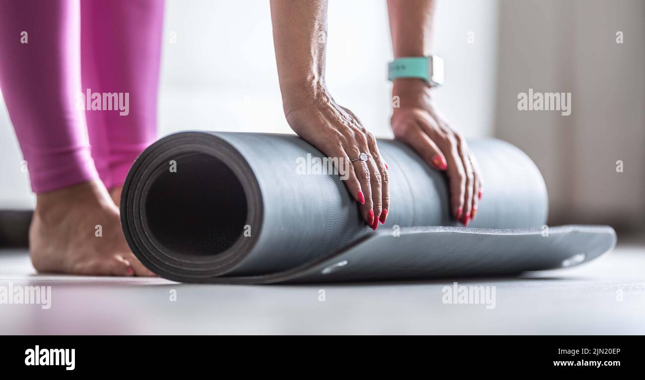 A woman rolls a mat before practicing yoga at home or in the gym. Stock Photo