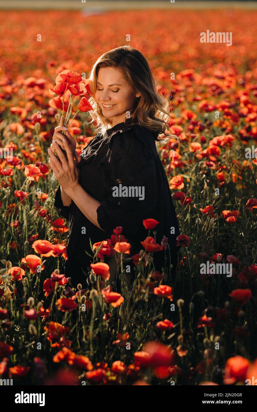 a girl in a black dress on a poppy field at sunset Stock Photo - Alamy