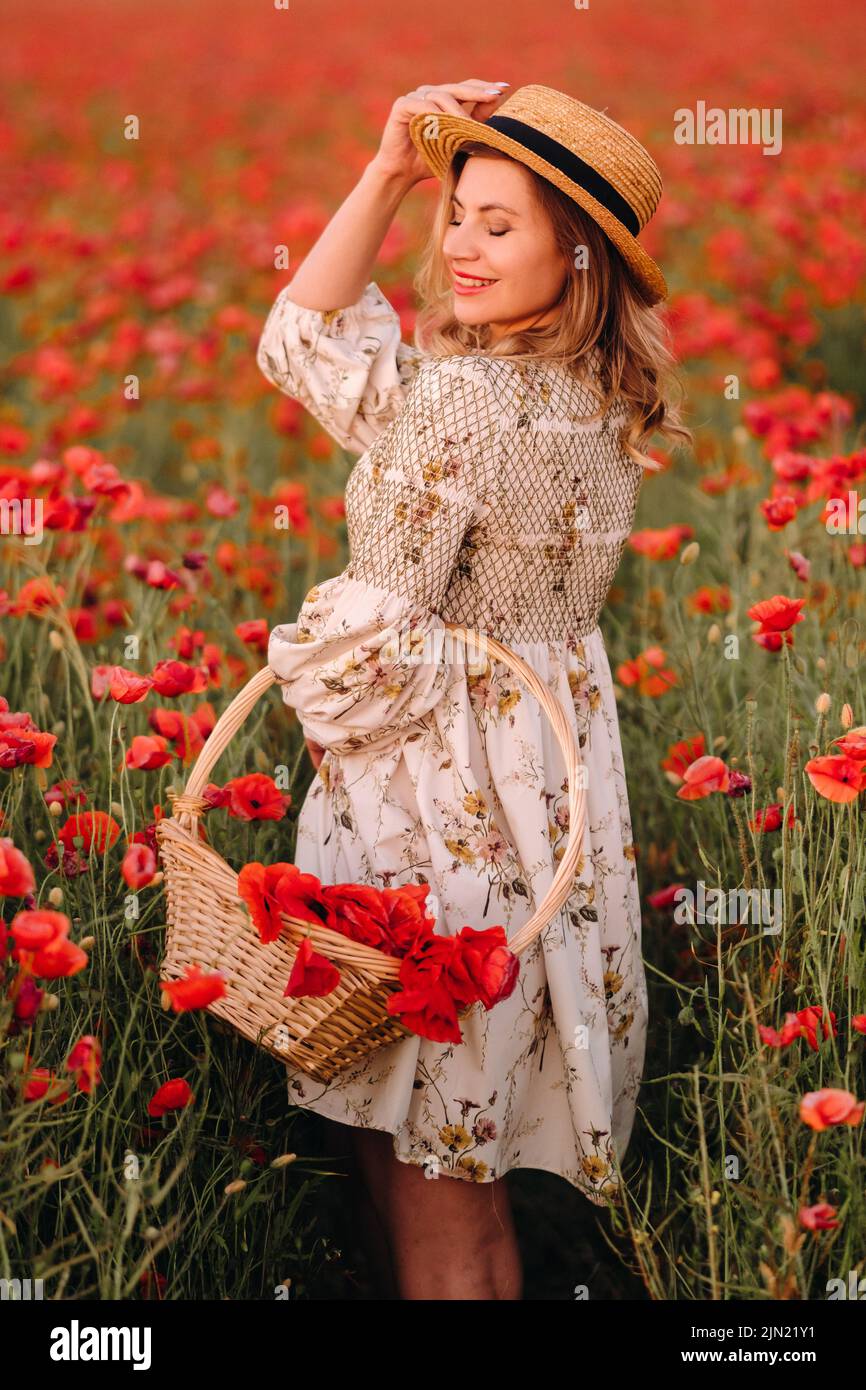 a girl in a dress with a hat and with a basket in a field with poppies. Stock Photo