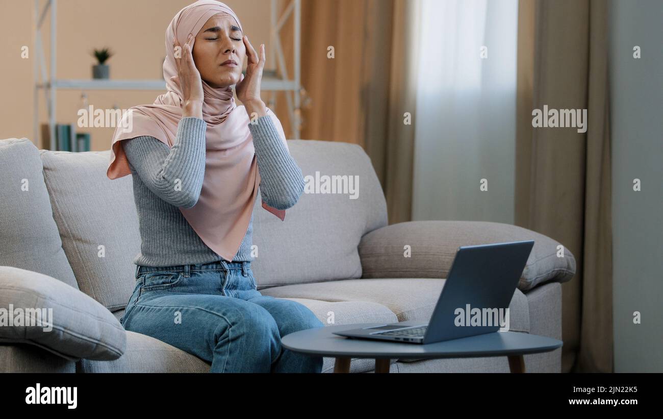 Young muslim woman in pink hijab sitting on sofa working using laptop ...