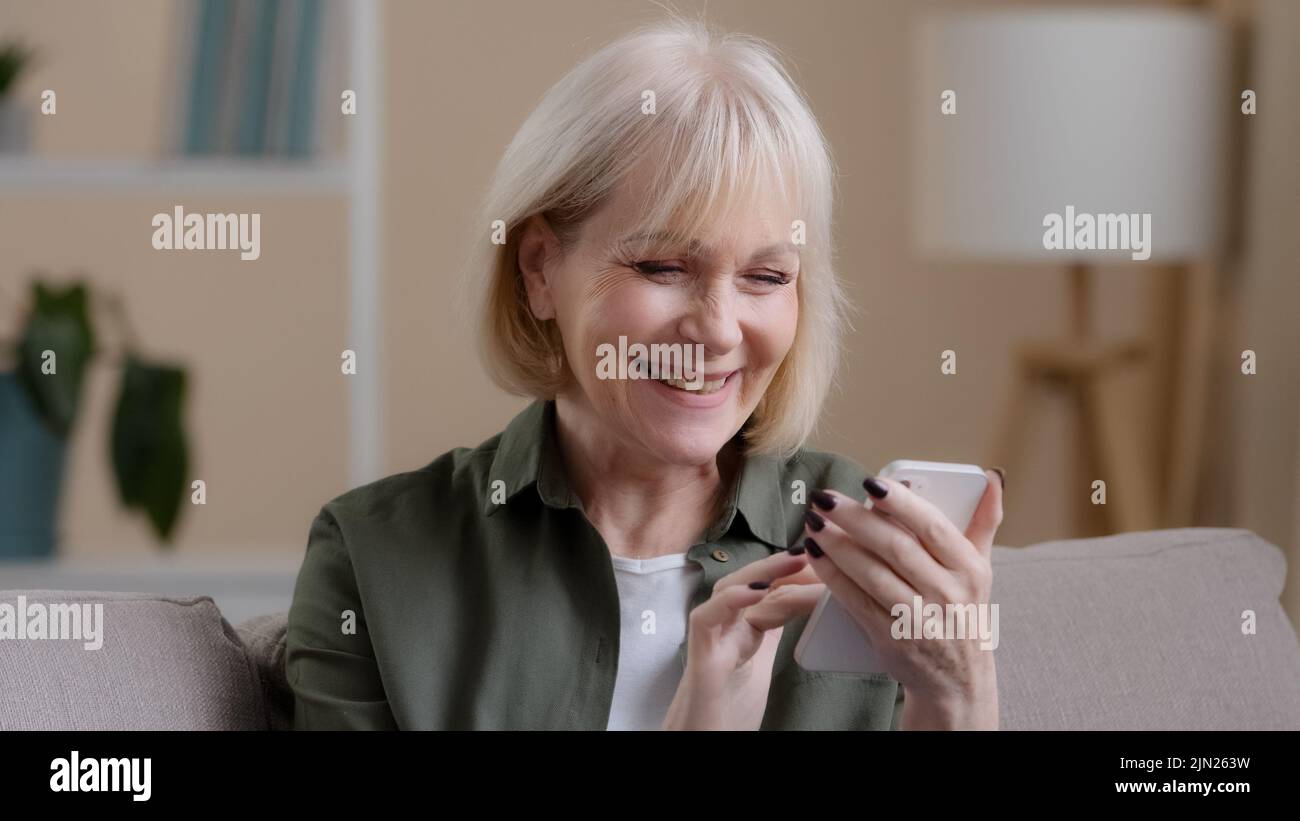 Close up happy smiling successful amazed old emotional woman receive good news offer money prize achievement with phone smiling rejoice showing thumb Stock Photo