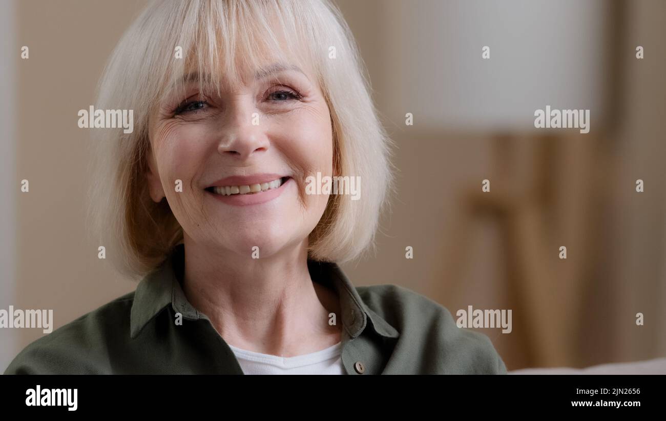Front view portrait mature blonde smiling caucasian woman looking at camera posing in studio portrait, cheerful older grey-haired female granny in Stock Photo