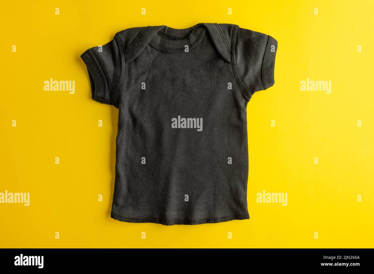 Flat lay mockup of a black t-shirt for a boy on a bright yellow background. Basic clothes for children made of natural fabric. Layout for design and p Stock Photo