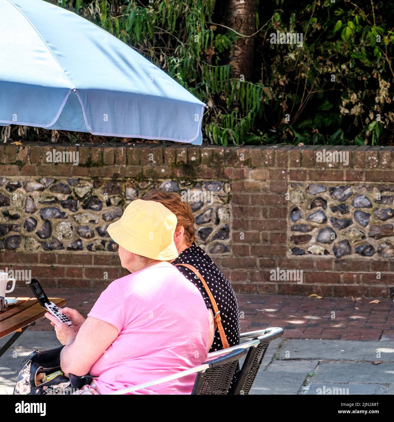 Dorking, Surrey Hills, London UK, July 07 2022, Older Woman Sitting With A Friend Using Mobile Phone Under Sun Shade Unbrella Stock Photo