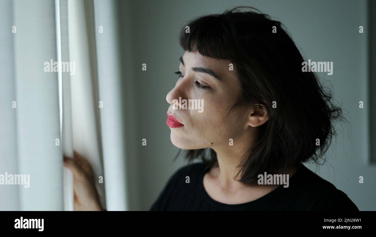 One hispanic woman peeking out through curtain window Stock Photo