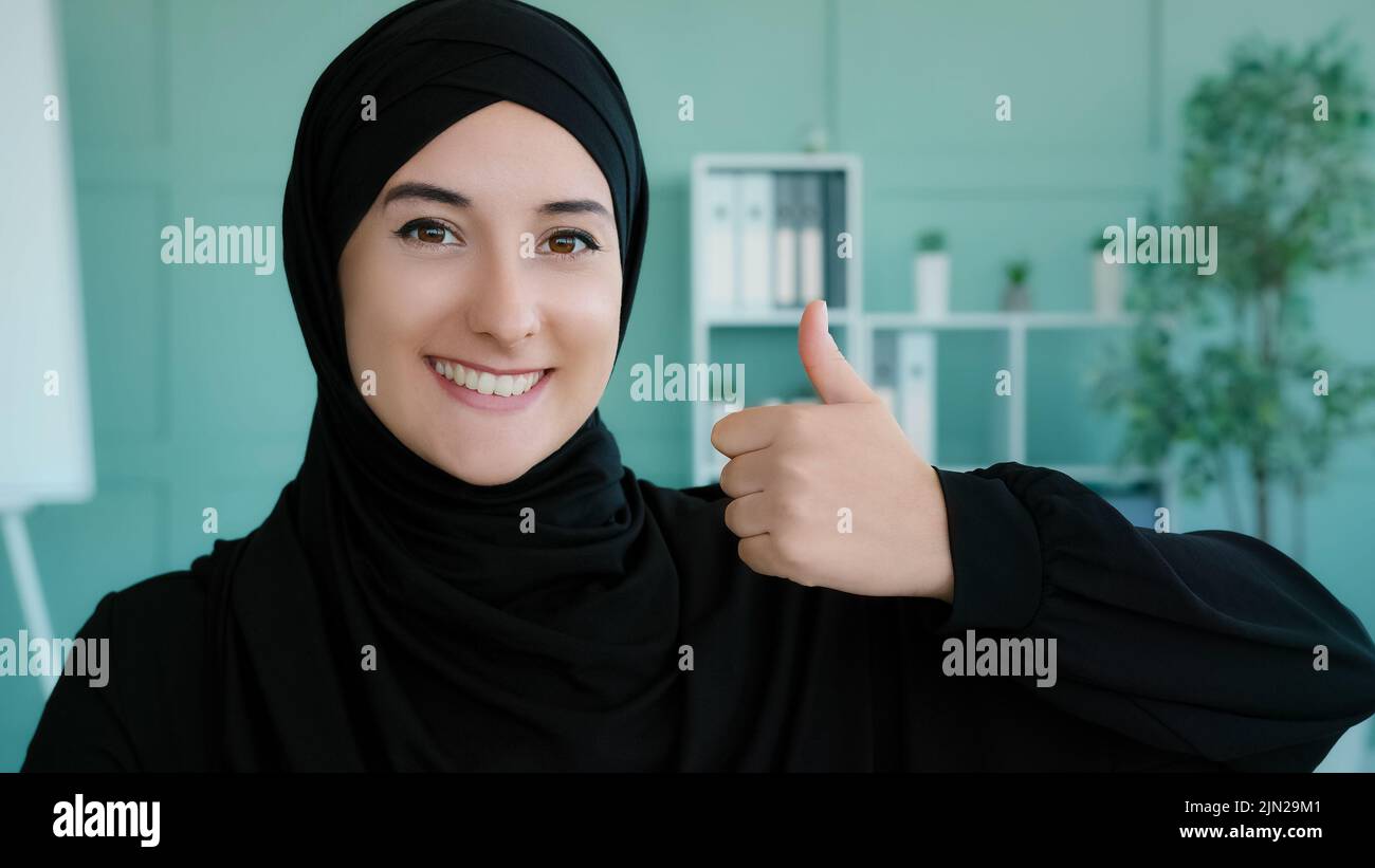 Close-up female portrait in office Muslim happy satisfied contented Islamic Arabian woman wearing black hijab looking at camera smiling toothy girl Stock Photo