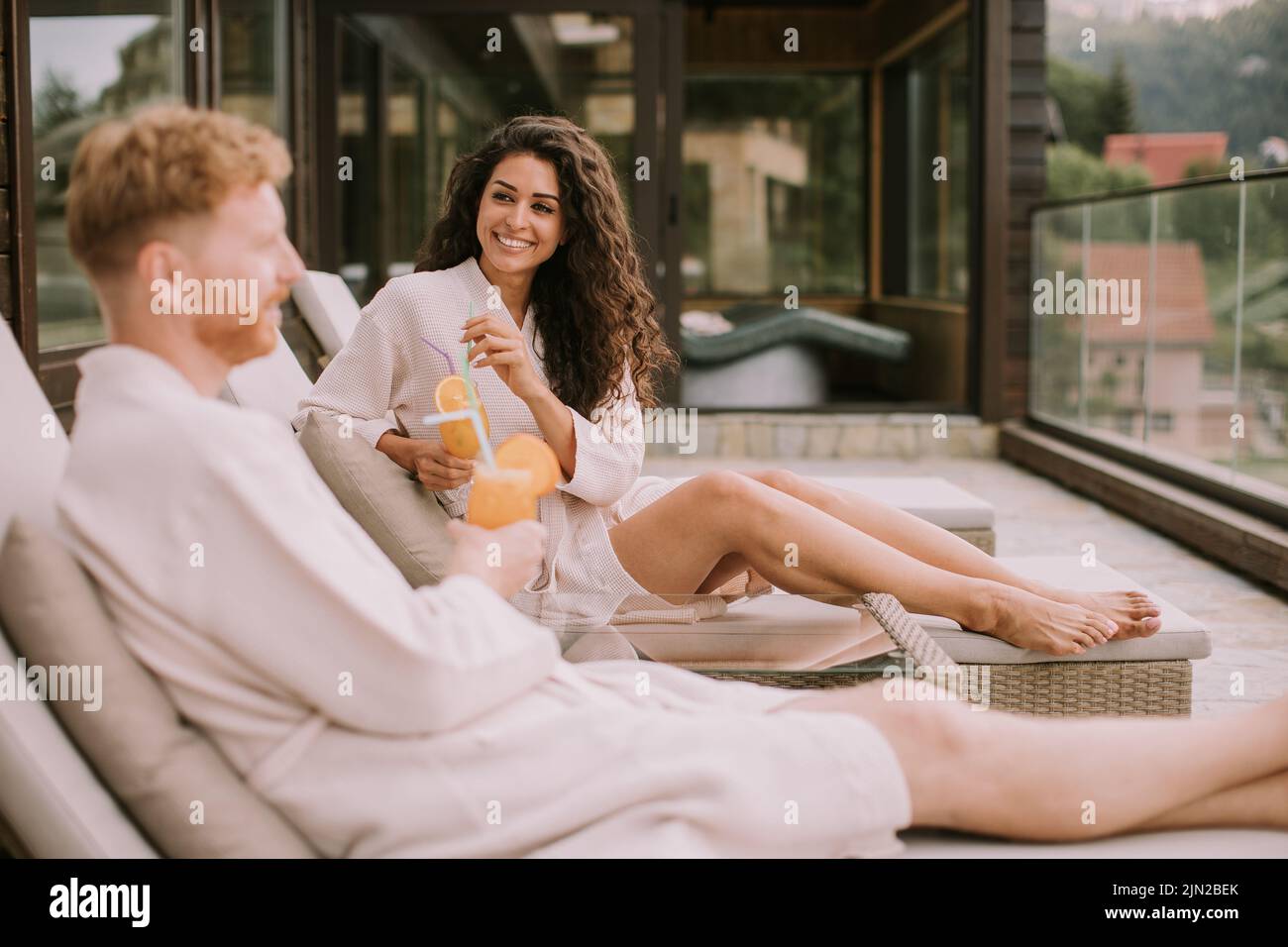 Handsome young couple relaxing on beds and drinking fresh orange juice on the outdoor terrace Stock Photo
