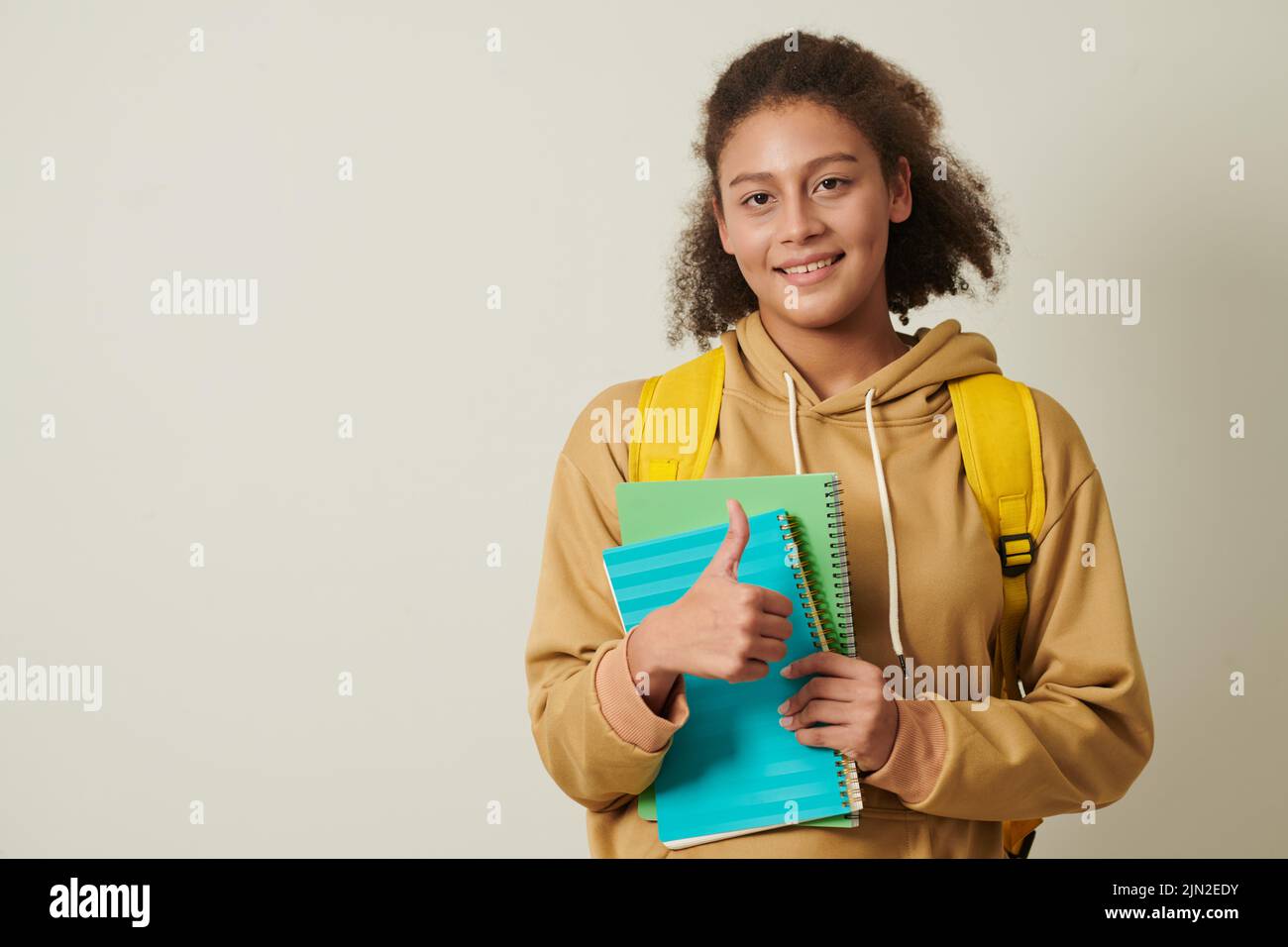 Portrait of smiling college student holding textbooks and showing ...