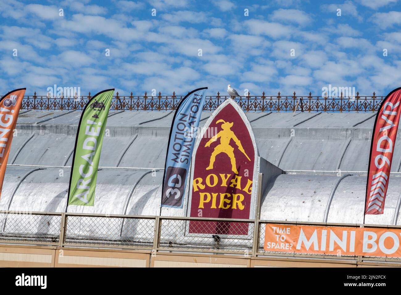 A section of roof on the Royal Pier, Aberystwyth, showing various banners and ornate ironwork. A seagull stands on the Royal Pier emblem. Stock Photo
