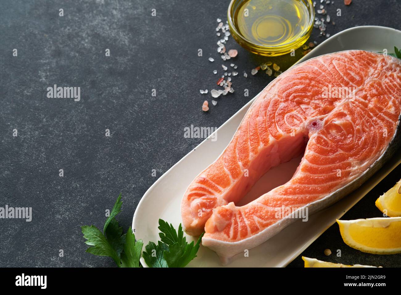 https://c8.alamy.com/comp/2JN2GR9/salmon-raw-salmon-steak-fresh-raw-salmon-fish-with-cooking-ingredients-herbs-and-lemon-prepared-for-grilled-baking-on-black-background-healthy-foo-2JN2GR9.jpg